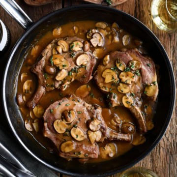 A skillet with three bone-in pork chops nestled in a luscious mushroom sauce.