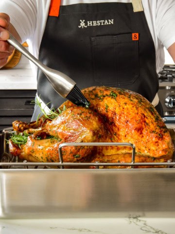 A side shot of a golden turkey getting baked in the roaster.