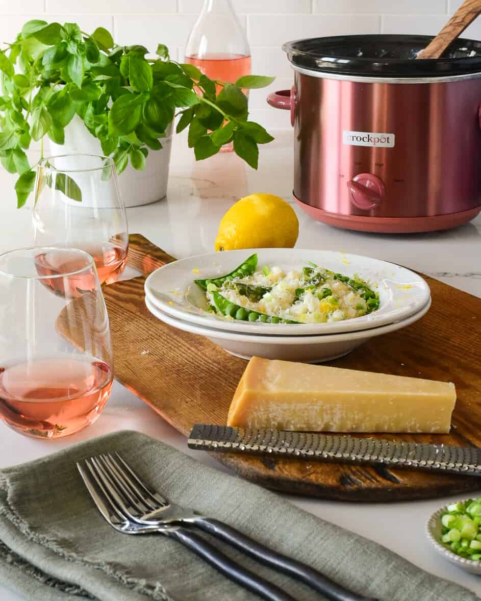 A plated bowl of a slow cooker spring risotto with asparagus and peas. With a rose copper Crockpot in the background.