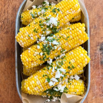 A pile of corn topped with a chili-lime butter, feta and cilantro in a galvanized tray.