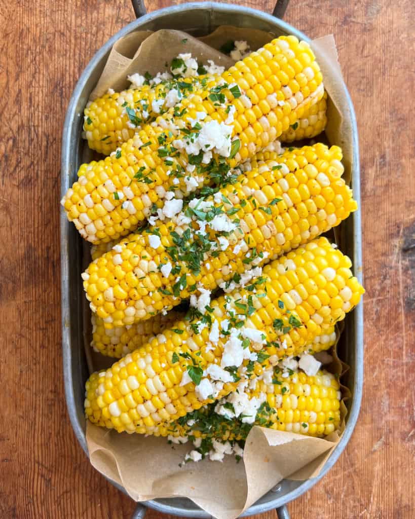 A pile of corn topped with a chili-lime butter, feta and cilantro in a galvanized tray.