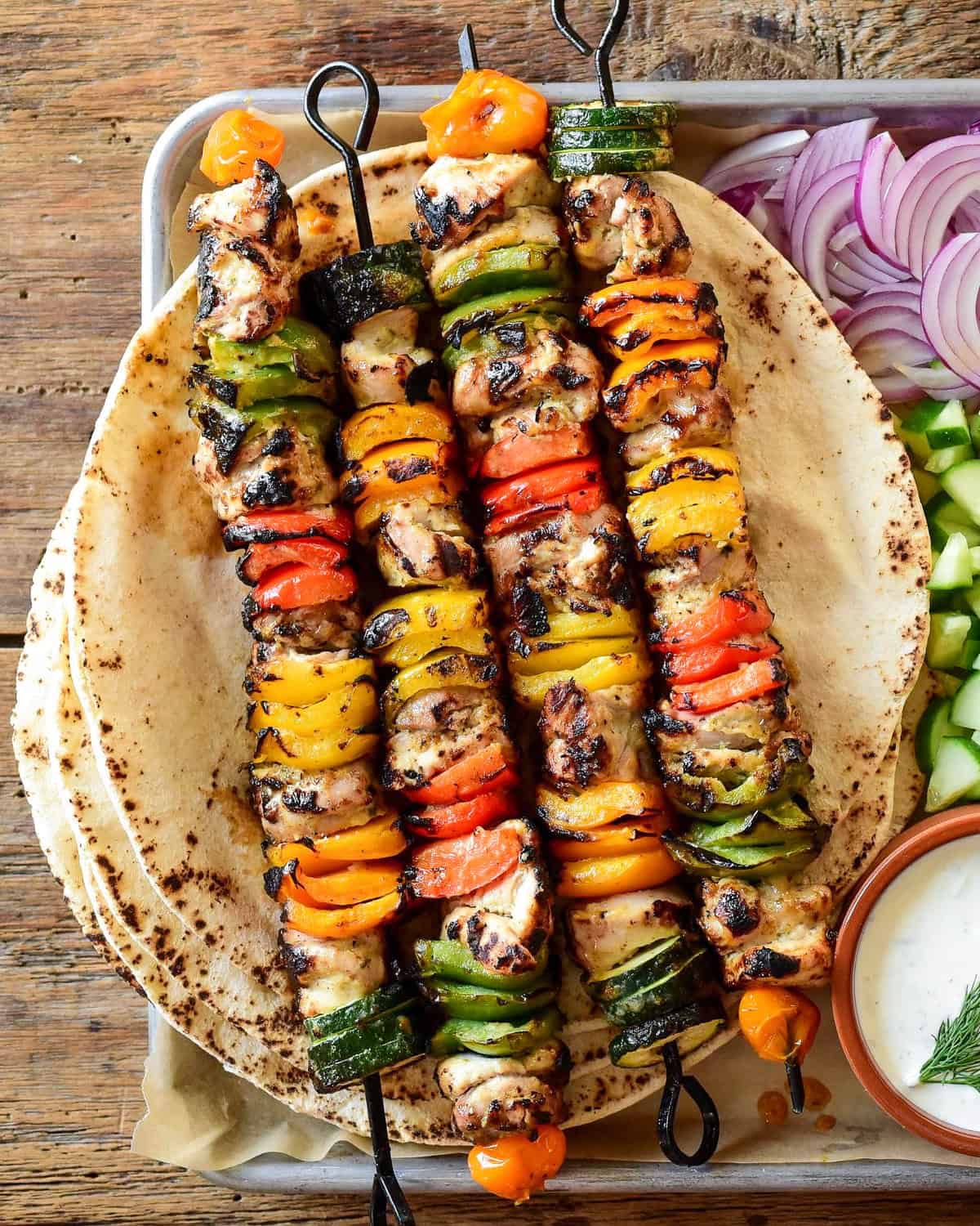 Four colourful grilled chicken and vegetable skewers served with pita.