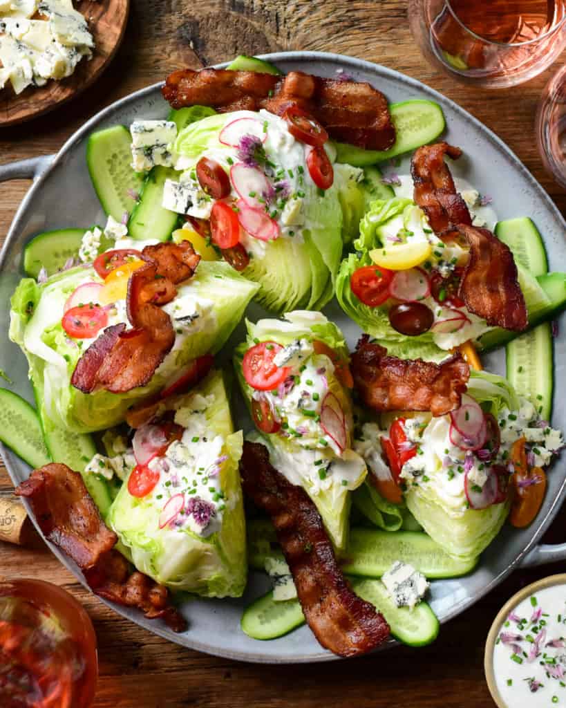A large wedge salad with six lettuce wedges topped with dressing, tomatoes and pieces of bacon.
