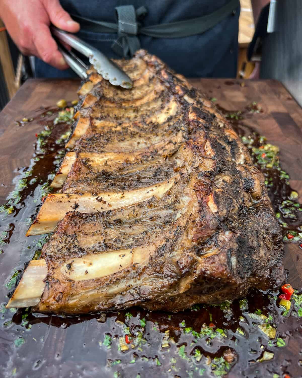 Seven grilled big ribs with a green salsa on a board with grilled garlic toast and a Caprese salad.
