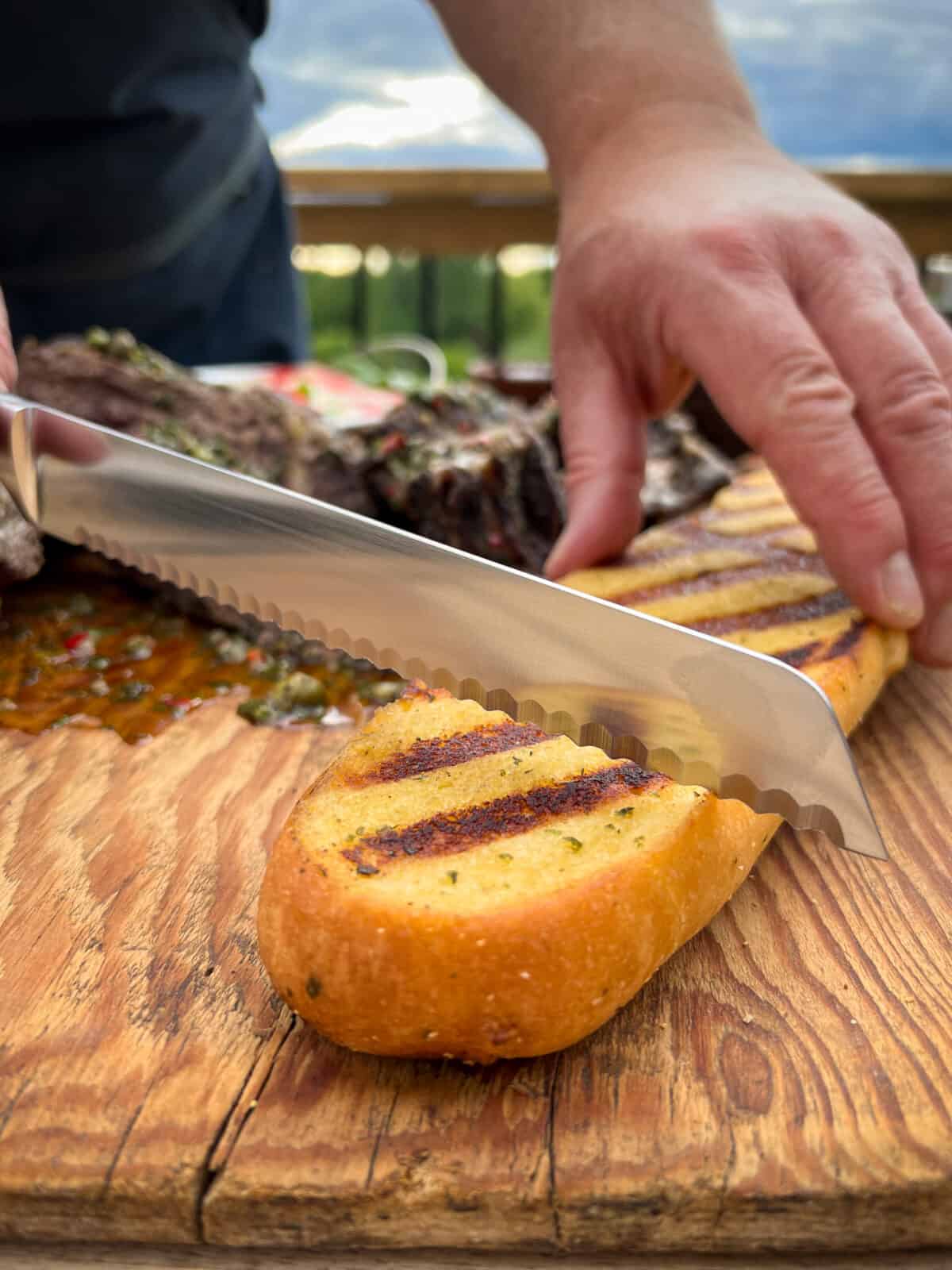 A loaf of garlic bread with grill marks being cut with a knife.