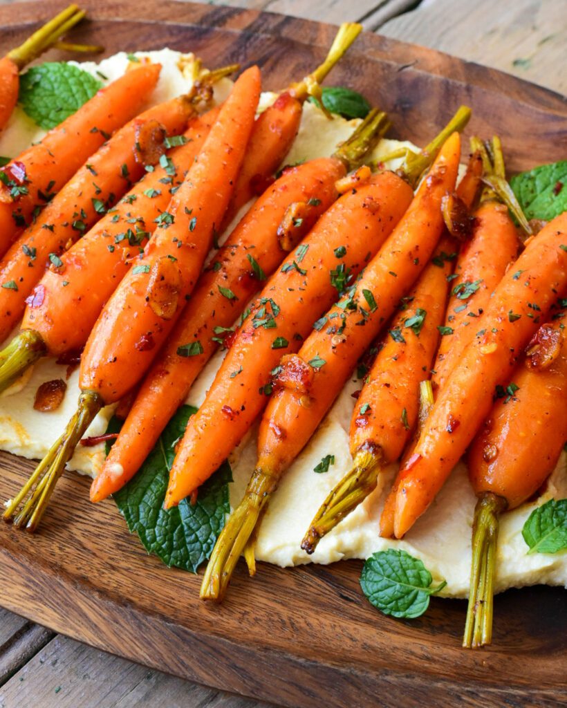 A platter of sous-vide carrots in a row on a bed of hummus.