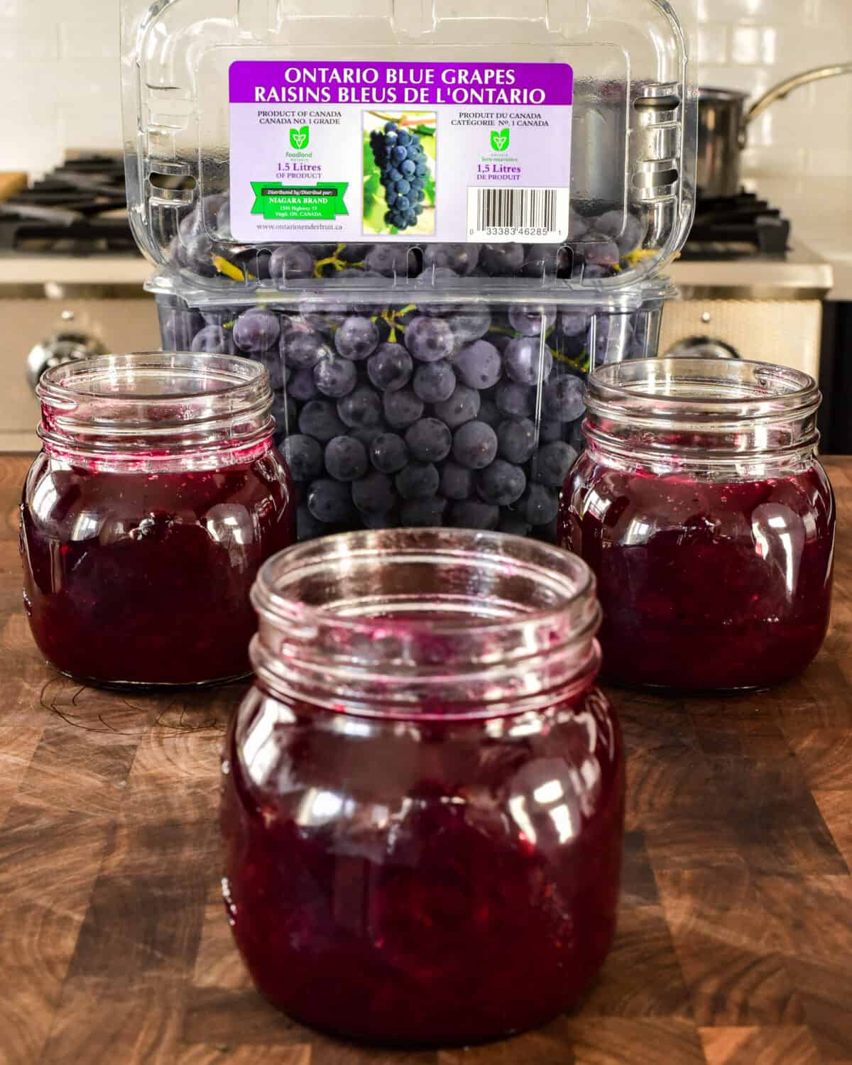 Three jars of jam in front of a container of Ontario Coronation grapes.