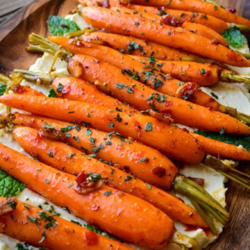 A platter of sous vide carrots on a bed of hummus and sprinkled with herbs.