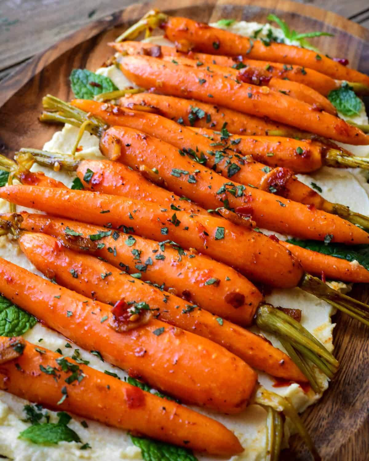 A platter of sous vide carrots on a bed of hummus and sprinkled with herbs.