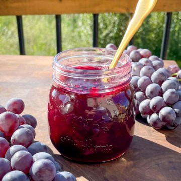 A jar of grape jam with with two bundles of Ontario grapes.