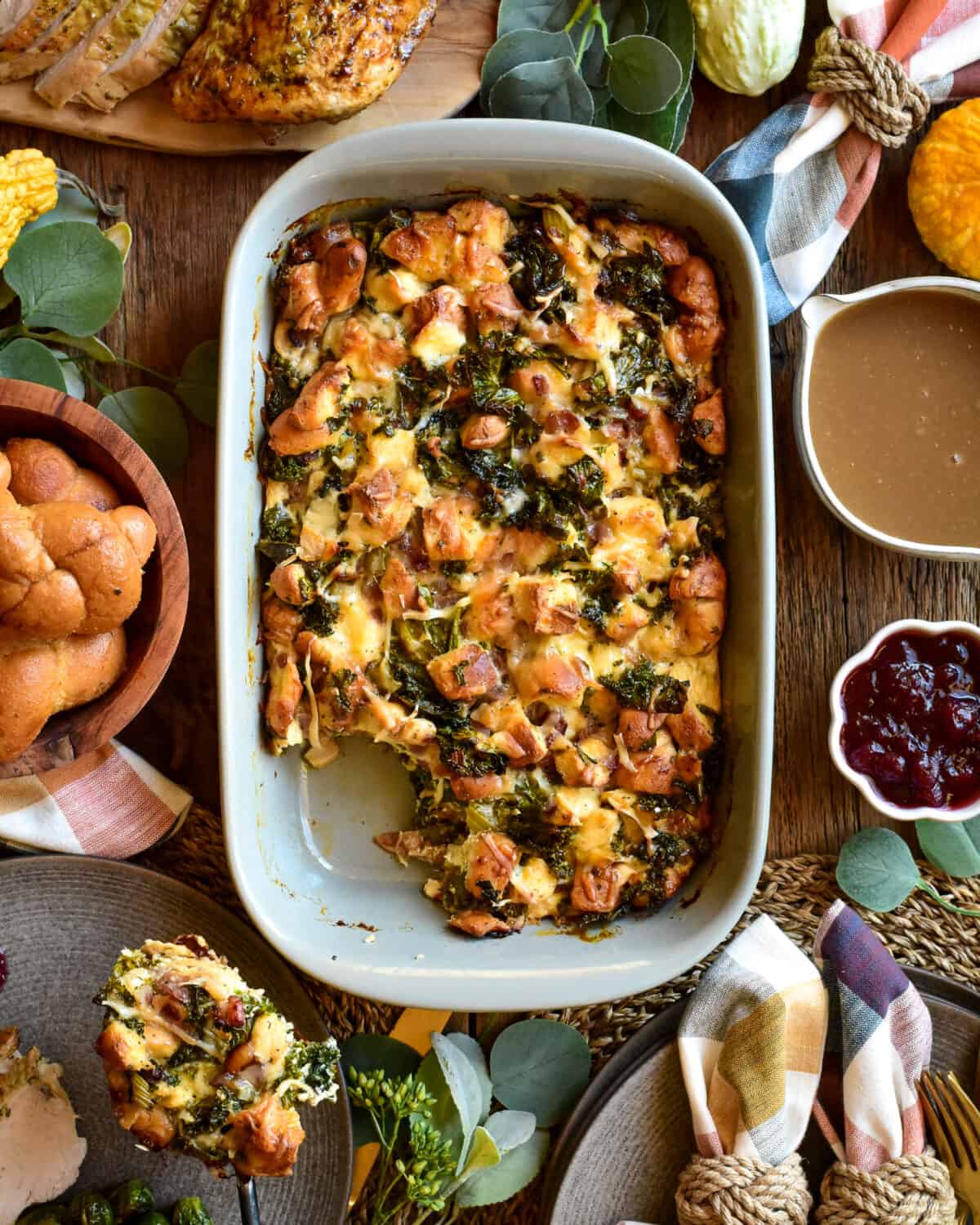 A Thanksgiving themed table setting with an oval dish of bread pudding in the center, with someone spooning out a portion onto a plate.