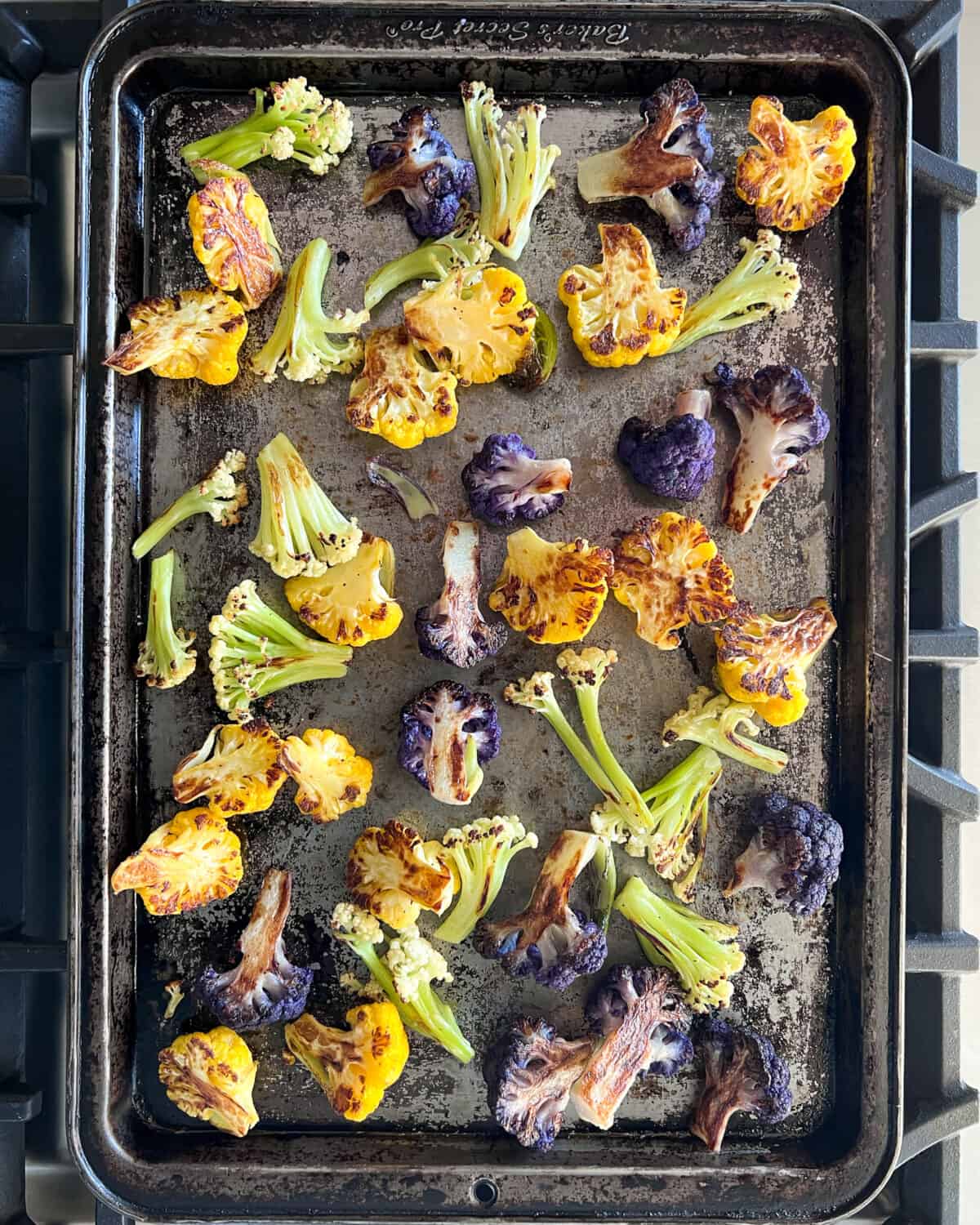 A top down image of purple, orange and caulilini cauliflower that was just roasted on a sheet pan.