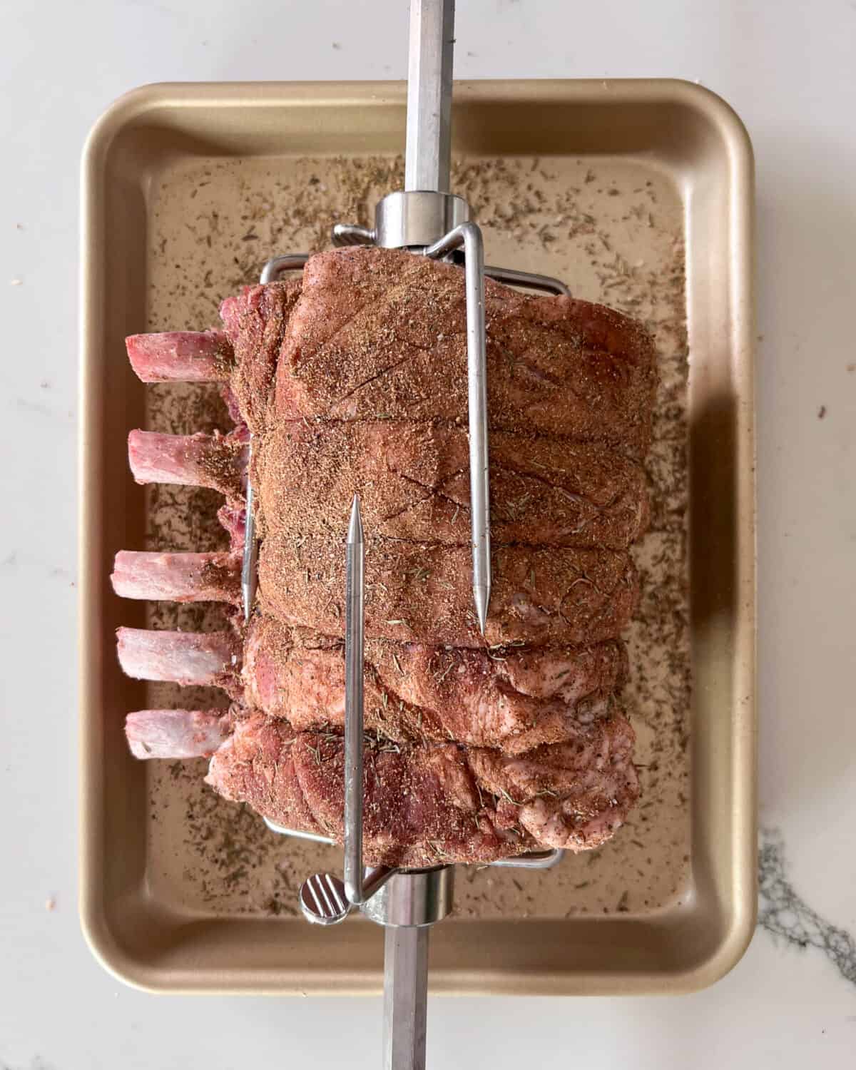 A pork roast is threaded onto the rotisserie rod and secured tightly with the forks.