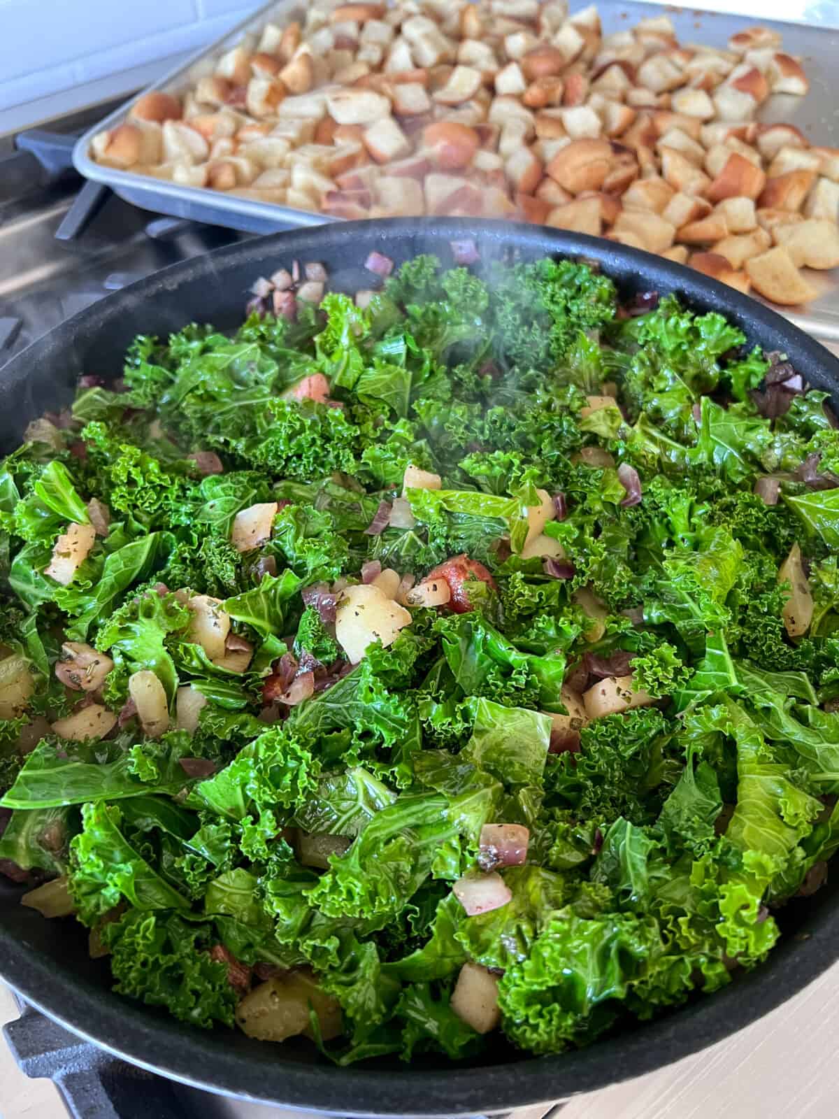 The vegetable kale mixture in a skillet with the toasted cubed bread in the background.