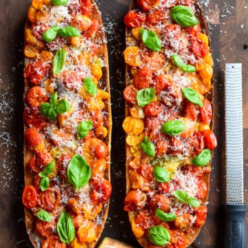 Two large half loaves of toast with tomato confit topped with grated parmesan and basil. A block of cheese and grater are beside the toast.