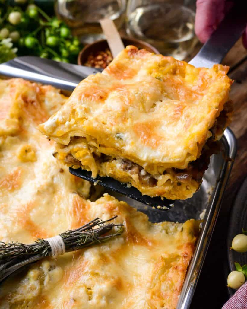 A piece of Butternut Squash and Turkey Sausage Lasagna is being lifted out of a baking pan.