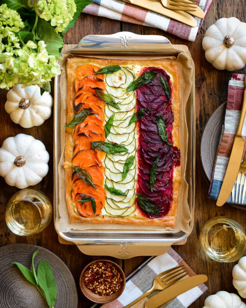 Puff pastry zucchini tart with rows of beets and sweet potatoes on a shiny sheet pan.