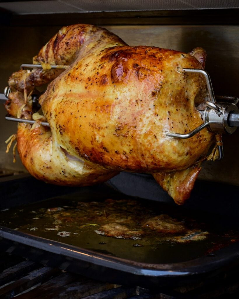 A golden brown chicken on a rotisserie at home on the grill.
