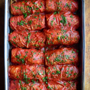 Two rows of cabbage rolls with tomato sauce in a baking pan.