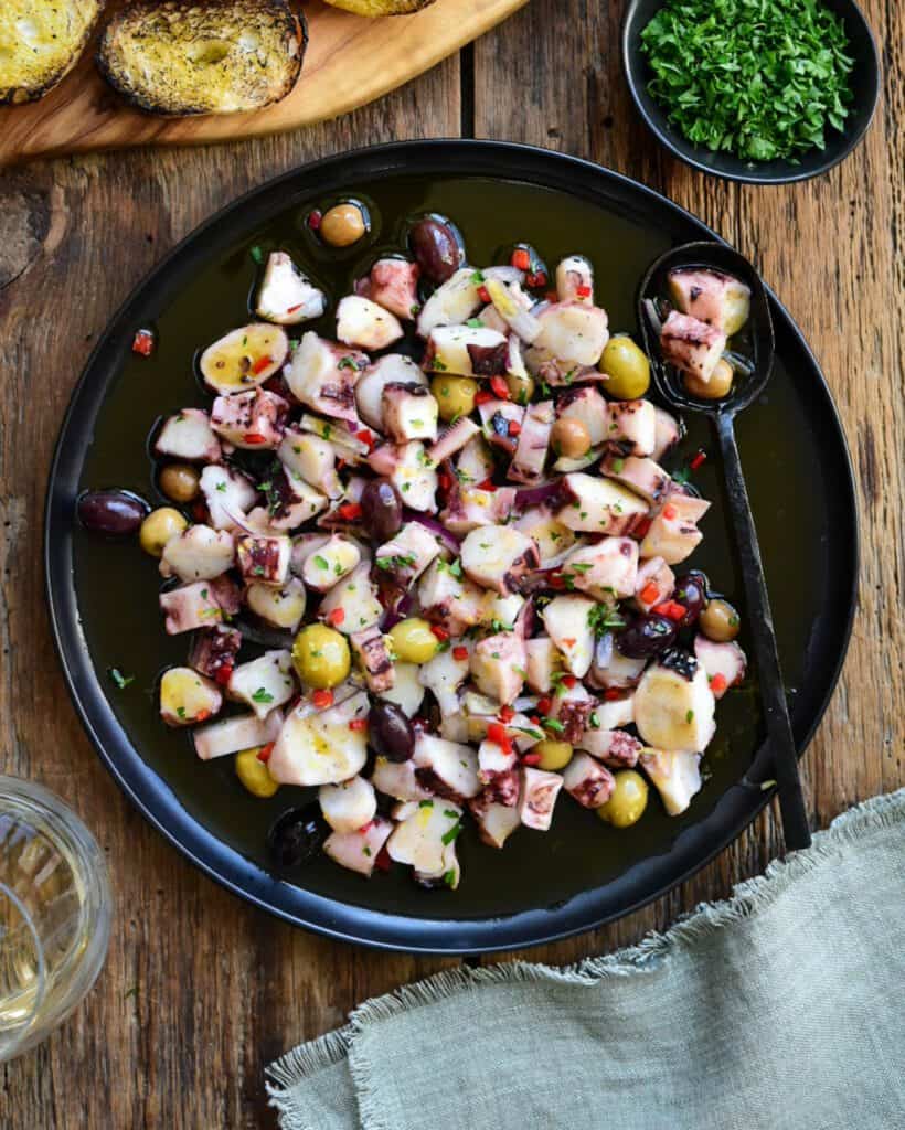 A marinated calamari salad on a black round plate.