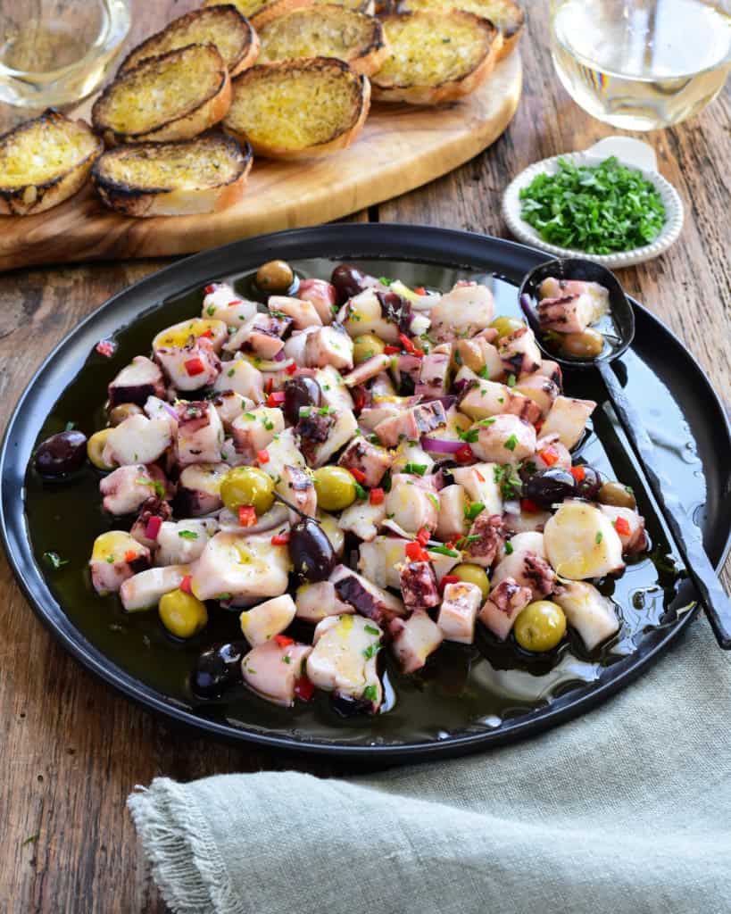 A Marinated Squid Salad with red peppers and olives served with toast and white wine.