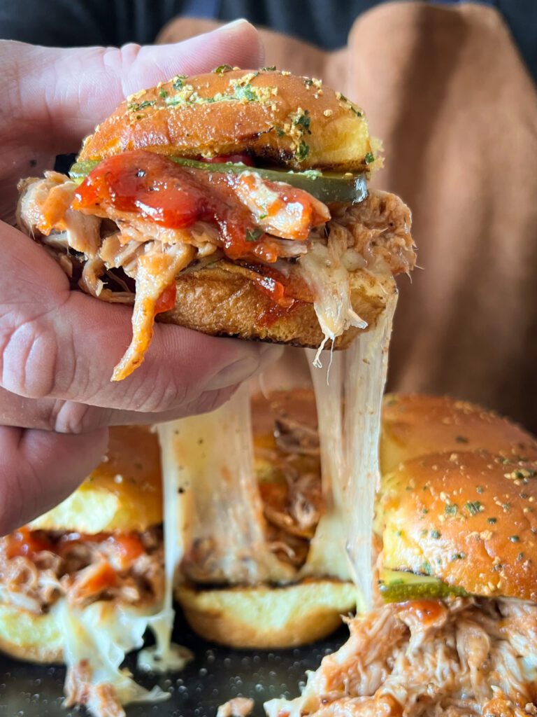 A pork slider getting lifted up with a cheese pull.
