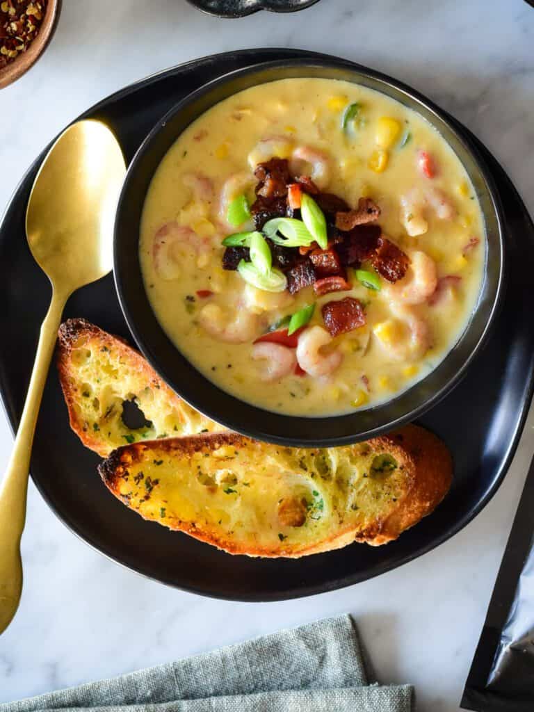 A bowl of bacon shrimp and corn chowder with two slices of toast.