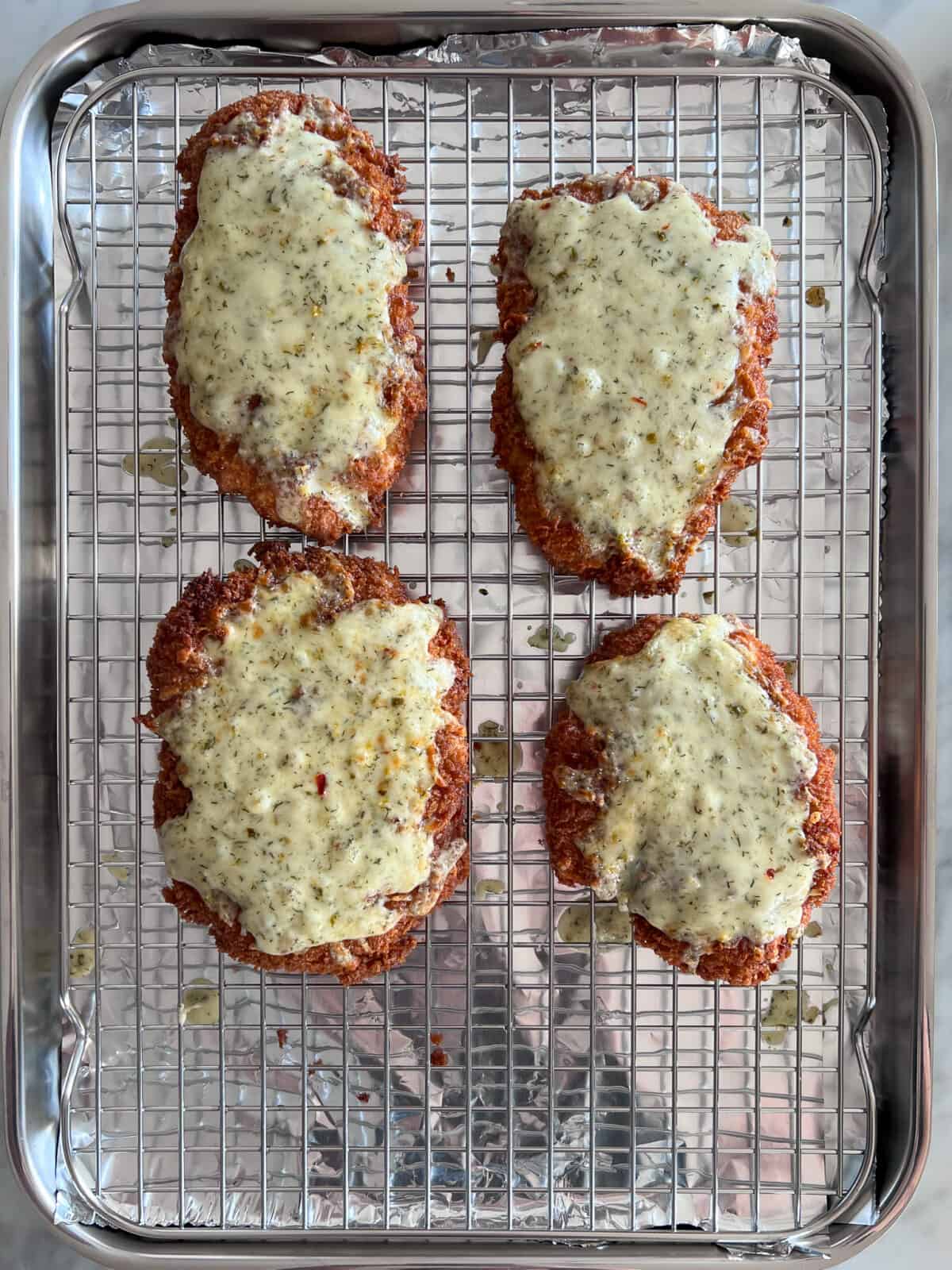 Four pieces of fried chicken with melted cheese on a rack.