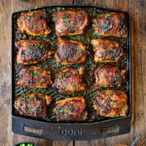 A top down image of twelve crispy chicken thighs on an Ooni Grizzler skillet.