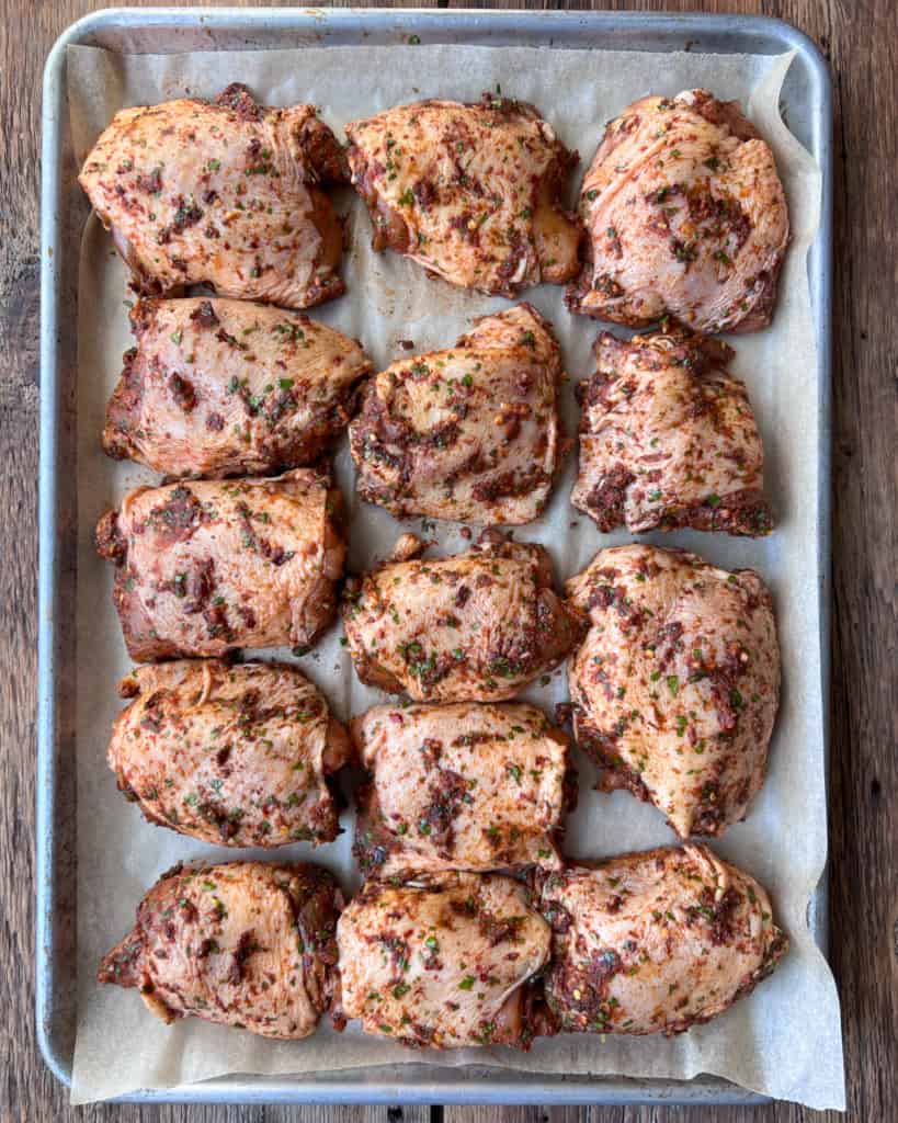 A sheet pan of raw marinated raw chicken thighs.