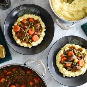 Two bowls and a pot of Guinness and Beef stew served with with mashed potatoes.