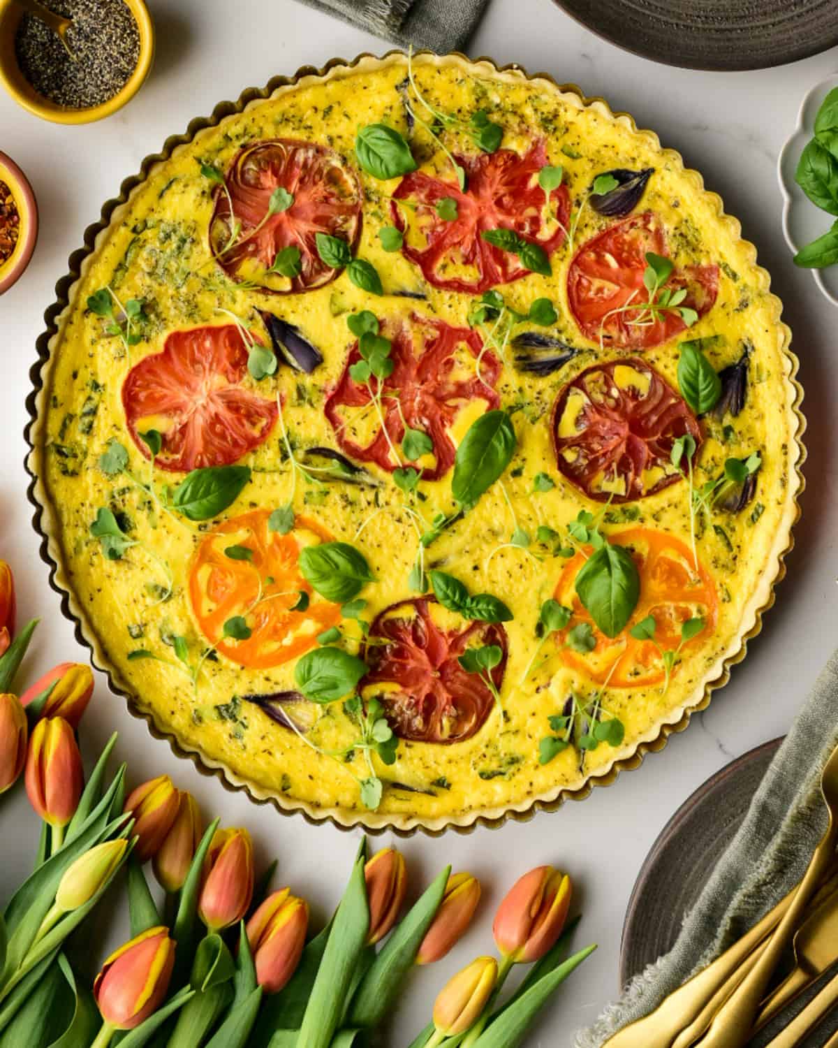 A spring Heirloom Tomato & Pearl Onion Quiche surrounded by tulips.