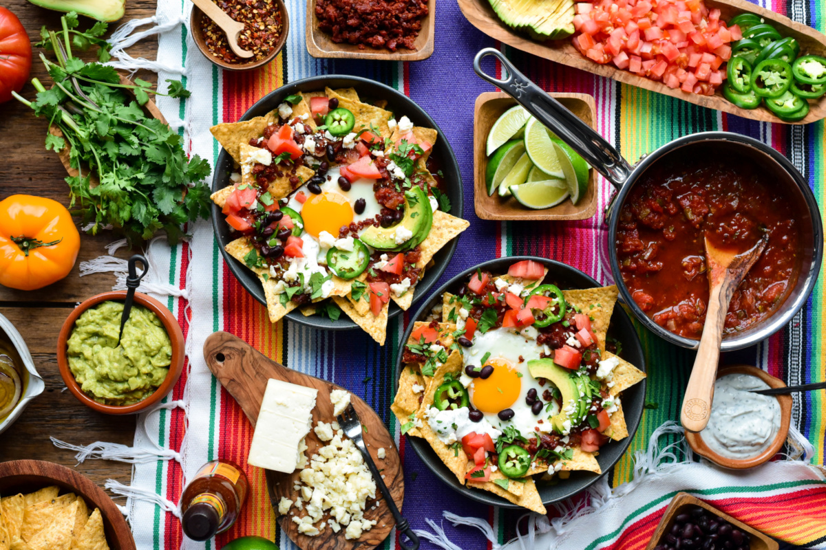 Two red chilaquiles breakfast bowls with a sunny-side-up egg and other various colourful toppings.