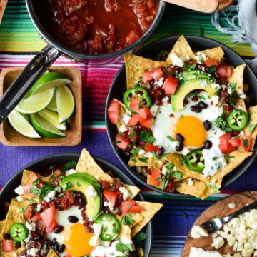 Two chilaquiles breakfast bowls with a sunny side up egg and other colourful toppings.