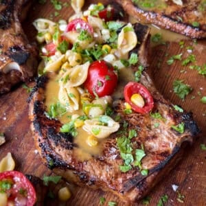 Grilled pork chop with a honey mustard sauce and a grilled corn and tomato pasta salad on top.