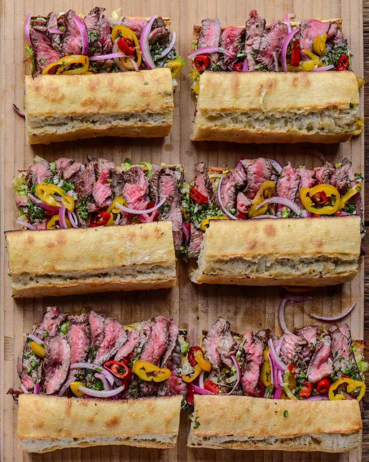 Six grilled steak sandwiches on baguettes.