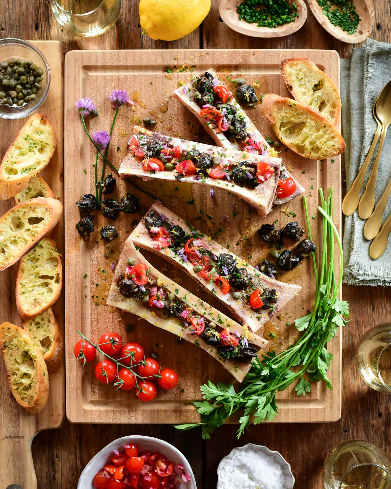 Four Bone Marrow bones with Garlic Butter Escargot, Tomatoes and Chive Flowers.