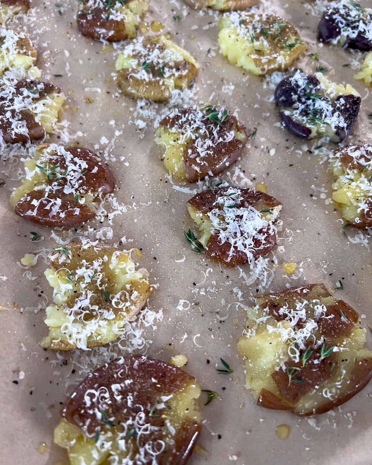 A tray of smashed potatoes sprinkled with parmesan cheese, fresh thyme, salt, pepper and garlic powder.