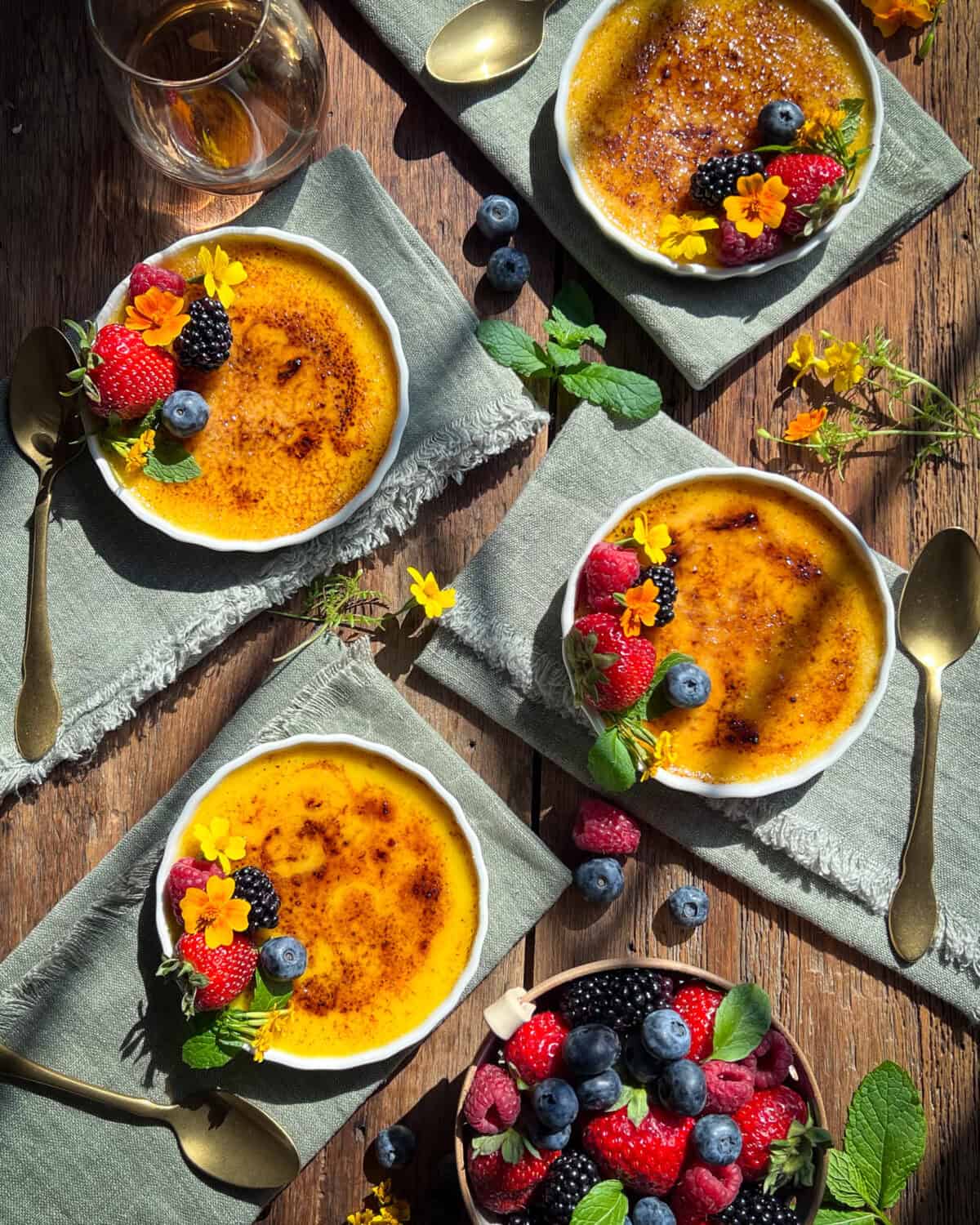 Four crème brûlée on napkins topped with berries and edible flowers.