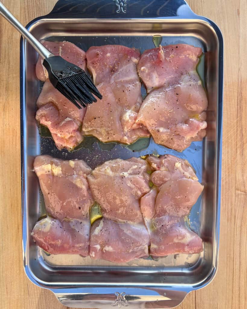 Six, skinless, boneless chicken thighs brushed with olive oil and salt and pepper on a sheet pan.