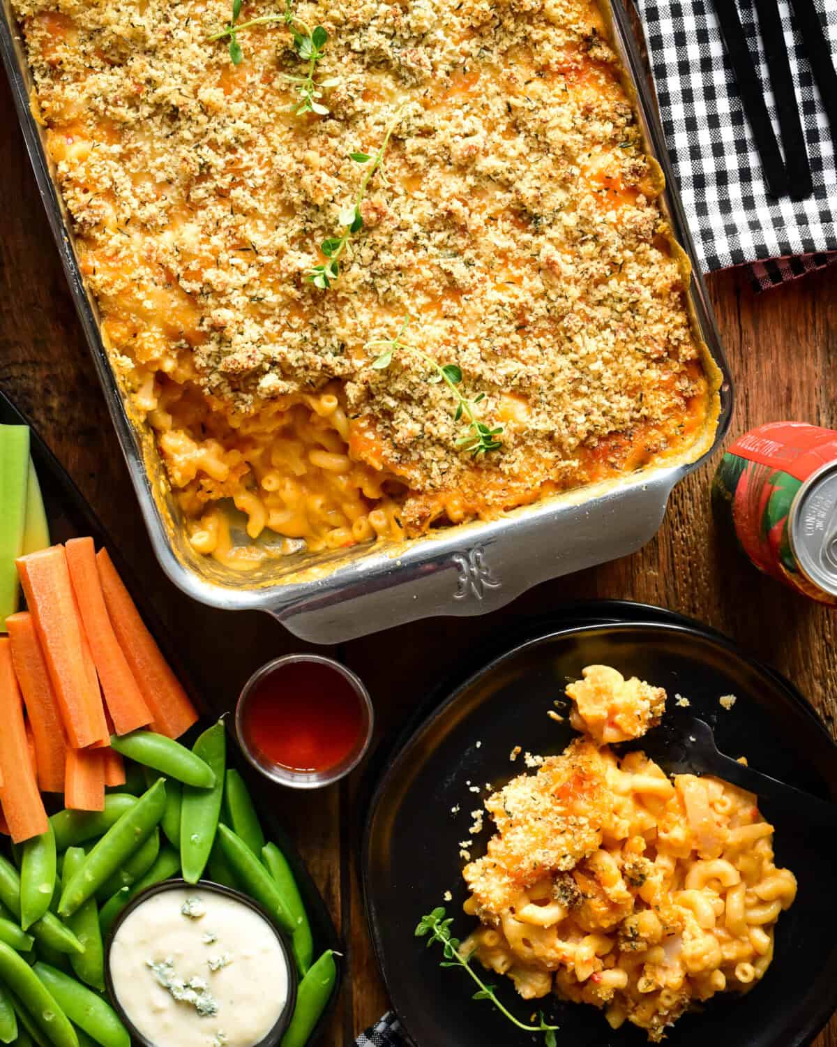 A tray of Buffalo Cauliflower Mac and Cheese with a portion on a plate. Served with crudités and blue cheese dip.