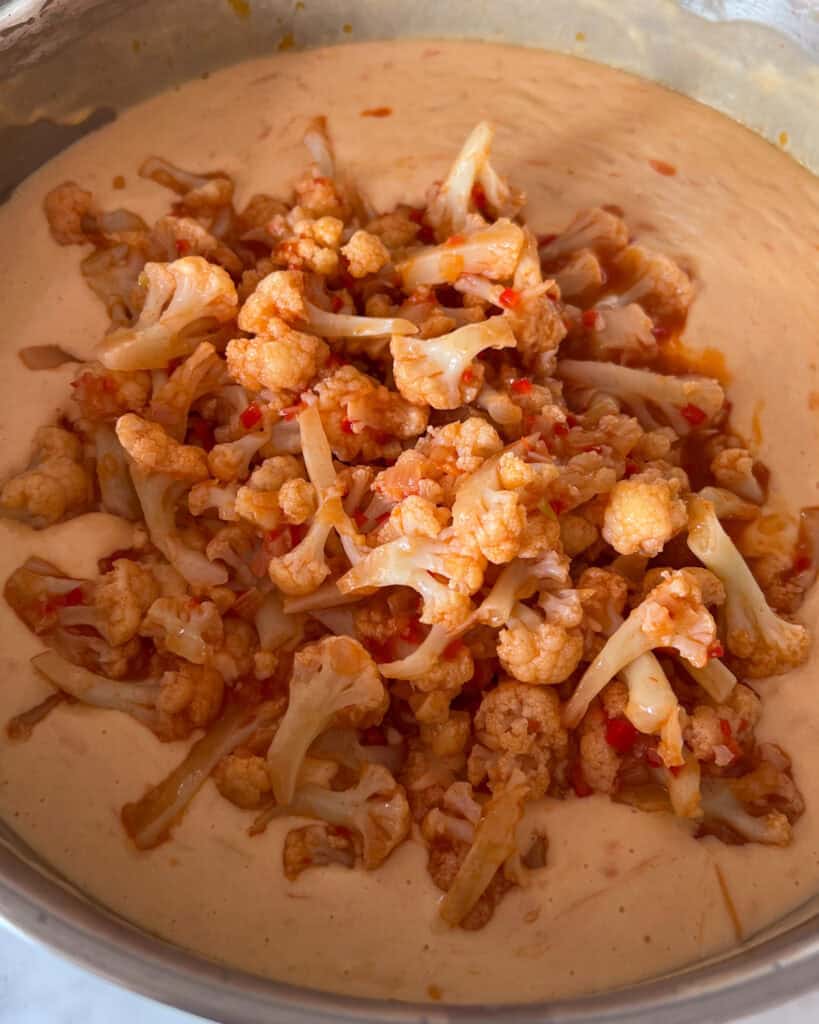 Adding the buffalo cauliflower to the cheese sauce.
