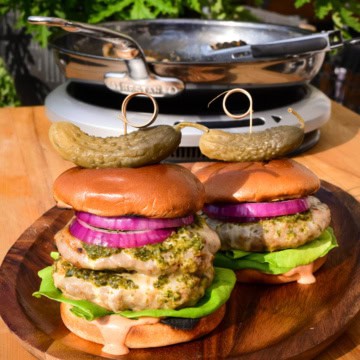 Two skillet burgers with chimichurri on a wooden plate. One is a double skillet cheeseburger.