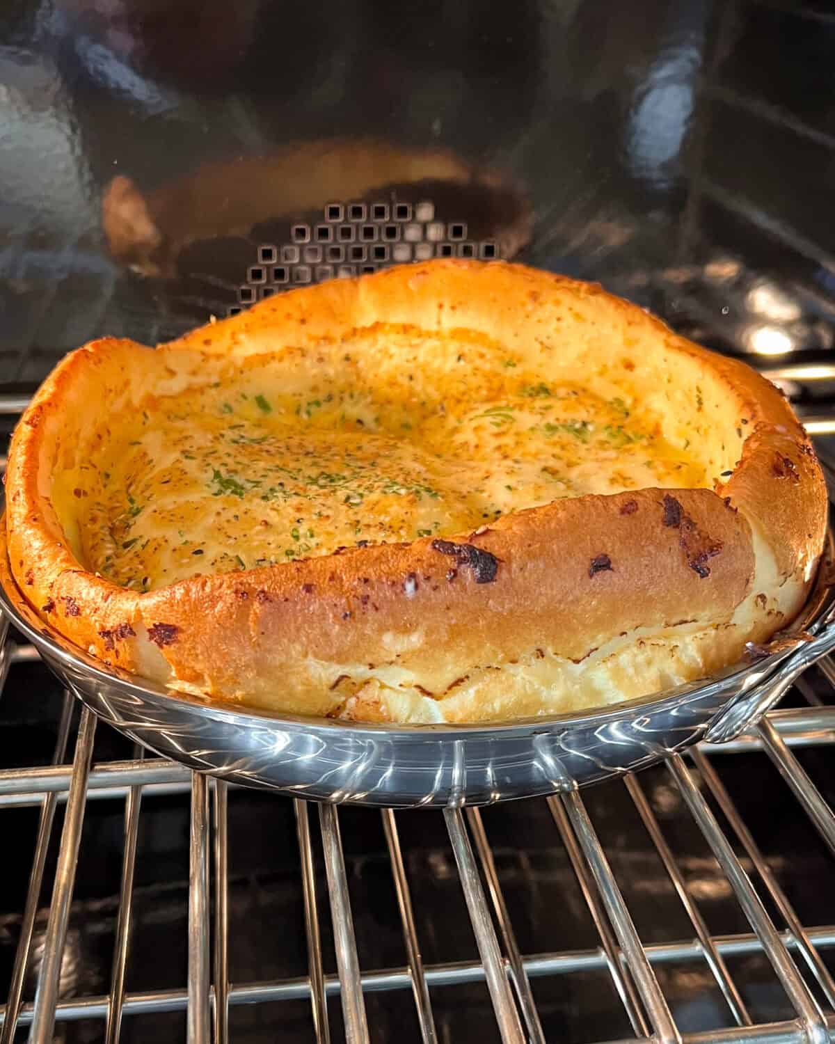 A Dutch baby in the oven with the pancake's edges risen higher than the center, creating a slightly sunken well in the middle,