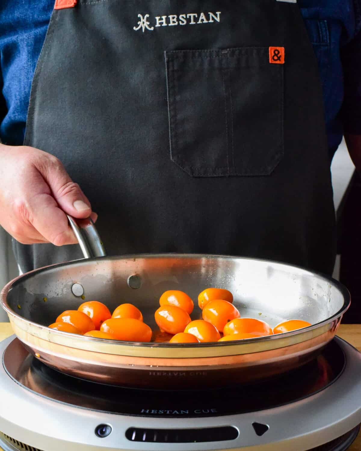 Blistering orange cherry tomatoes in a skillet.