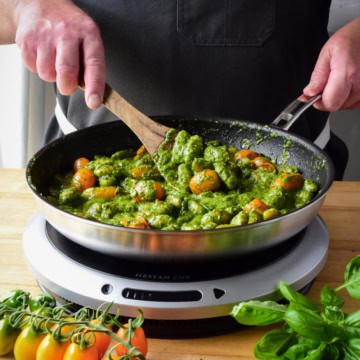A chef stirring a pan of fried pesto with orange tomatoes on a portable induction burner.