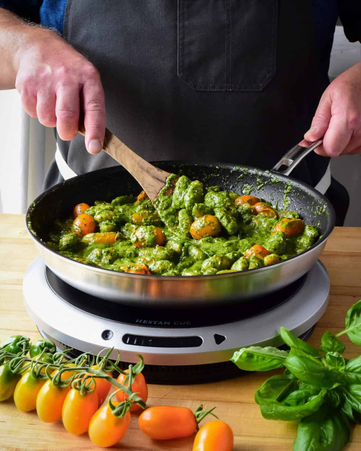 A chef stirring a pan of fried pesto with orange tomatoes.