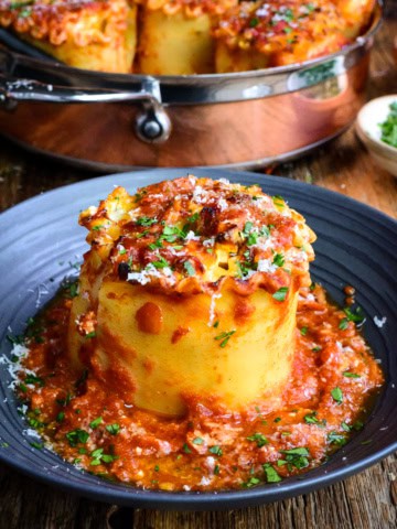 Close-up of a butternut squash lasagna roll-up topped with marinara sauce and herbs, served on a black plate.