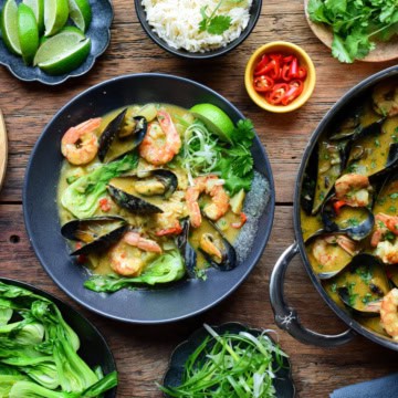 A bowl of yellow curry with shrimp and mussels, served with rice, green onions, cilantro, a lime wedge and served with warm naan.