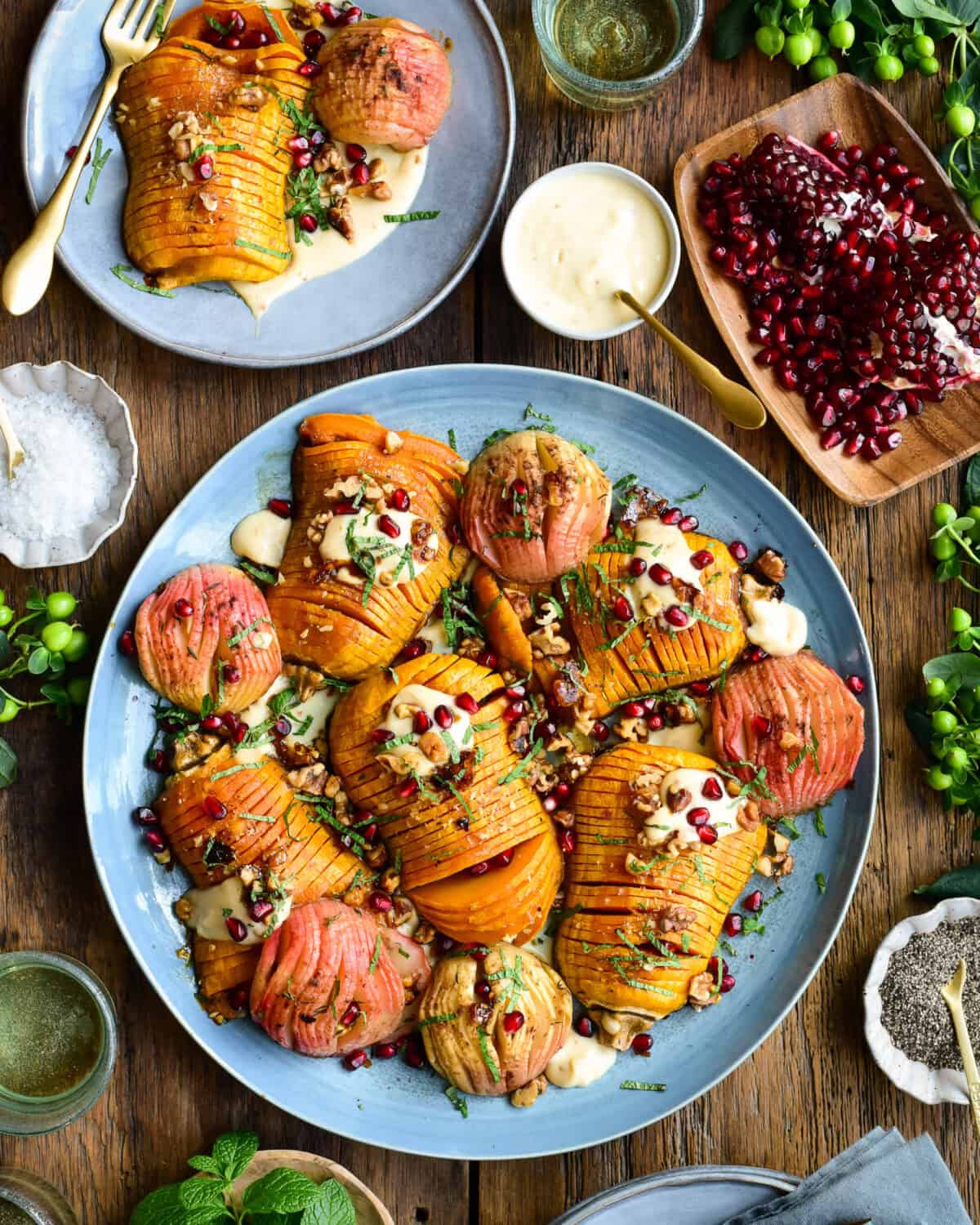 Hasselback Honeynut Squash and Apples, served on a platter or individual plates. Garnished with pomegranite arils, dressing, walnuts and chopped mint.